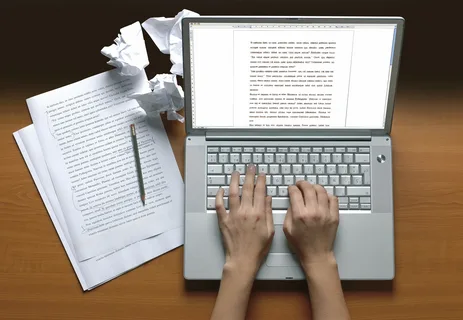 "Person working on a writing assignment at a desk with a laptop and notes